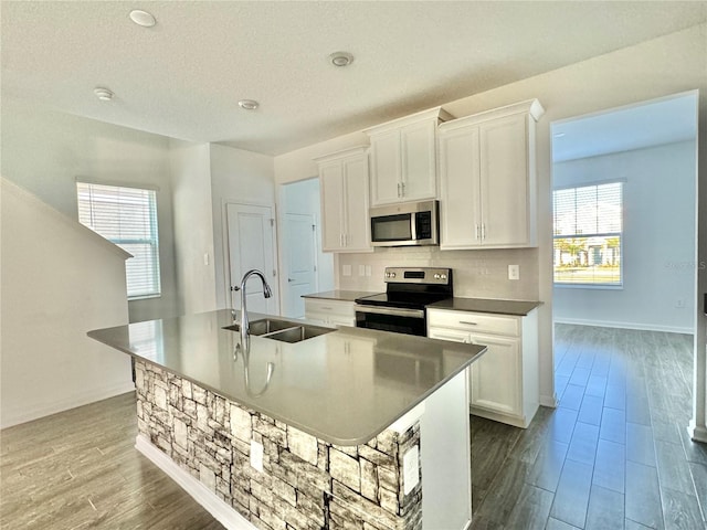 kitchen with a kitchen island with sink, white cabinets, sink, appliances with stainless steel finishes, and light hardwood / wood-style floors