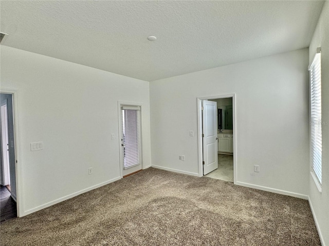 unfurnished bedroom with a textured ceiling, ensuite bathroom, and light carpet