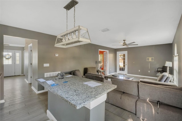 kitchen with light hardwood / wood-style floors, light stone counters, hanging light fixtures, and ceiling fan