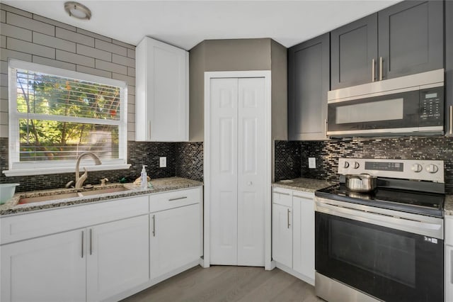 kitchen featuring white cabinets, sink, light hardwood / wood-style flooring, light stone countertops, and stainless steel appliances