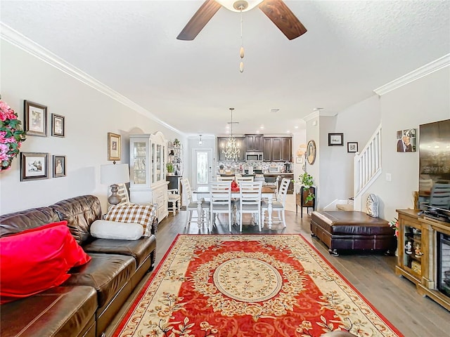 living room with ceiling fan with notable chandelier, wood-type flooring, and crown molding