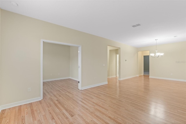 empty room featuring a notable chandelier and light hardwood / wood-style floors