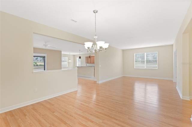 spare room with ceiling fan with notable chandelier, plenty of natural light, and light hardwood / wood-style floors