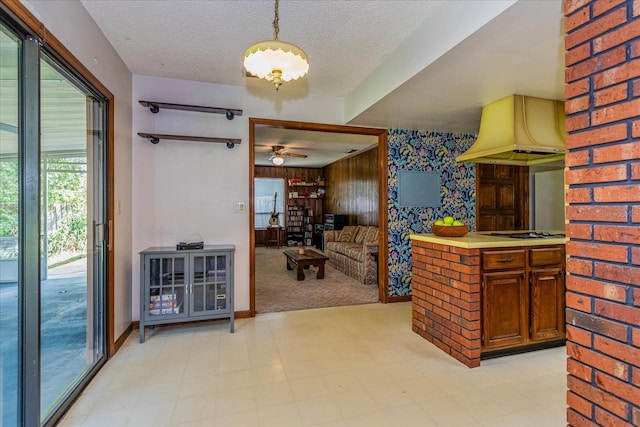 kitchen featuring premium range hood, light carpet, hanging light fixtures, ceiling fan, and a textured ceiling