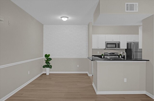 kitchen with stainless steel appliances, dark countertops, visible vents, light wood-style flooring, and white cabinetry