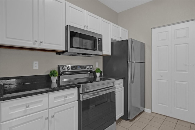 kitchen featuring dark stone countertops, stainless steel appliances, light tile patterned flooring, and white cabinetry