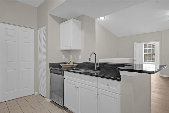 kitchen with white cabinets, a sink, dark stone countertops, dishwasher, and a peninsula