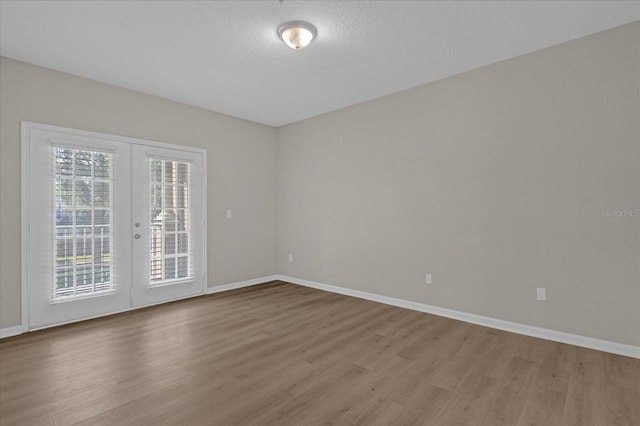 spare room with french doors, a textured ceiling, baseboards, and wood finished floors