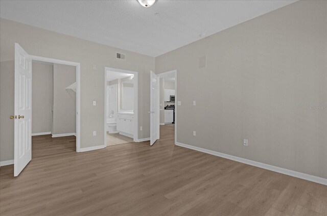 unfurnished bedroom with light wood-type flooring, visible vents, ensuite bath, and baseboards