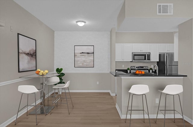 kitchen featuring visible vents, dark countertops, appliances with stainless steel finishes, a breakfast bar area, and white cabinetry