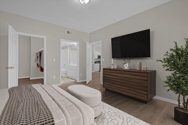 bedroom with ensuite bath, wood finished floors, visible vents, and baseboards