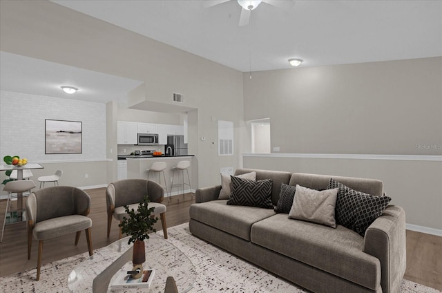 living area featuring lofted ceiling, visible vents, ceiling fan, light wood-type flooring, and baseboards