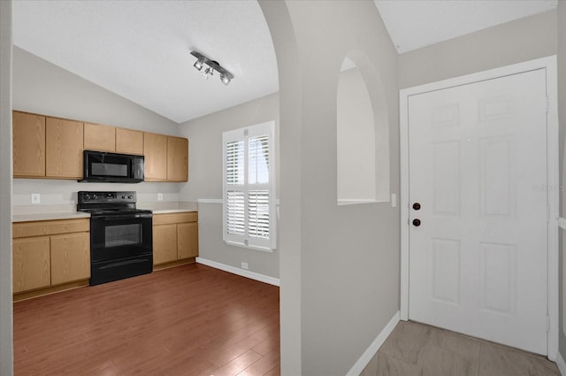 kitchen with black appliances, light brown cabinets, light wood-type flooring, and lofted ceiling