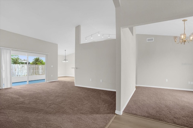 carpeted empty room with a notable chandelier, vaulted ceiling, and track lighting