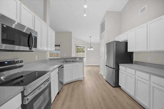 kitchen with white cabinets, hanging light fixtures, vaulted ceiling, light hardwood / wood-style floors, and stainless steel appliances