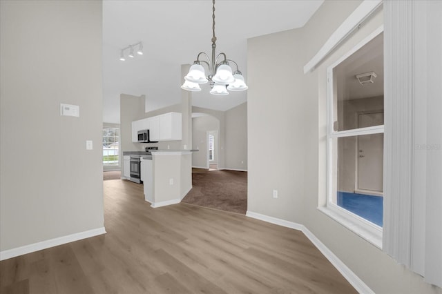 unfurnished dining area featuring a notable chandelier, light wood-type flooring, rail lighting, and vaulted ceiling