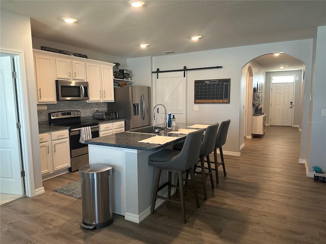 kitchen featuring stainless steel appliances, dark hardwood / wood-style flooring, a center island with sink, white cabinets, and a barn door