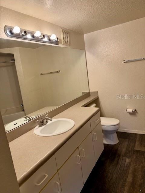 bathroom featuring walk in shower, vanity, a textured ceiling, hardwood / wood-style flooring, and toilet