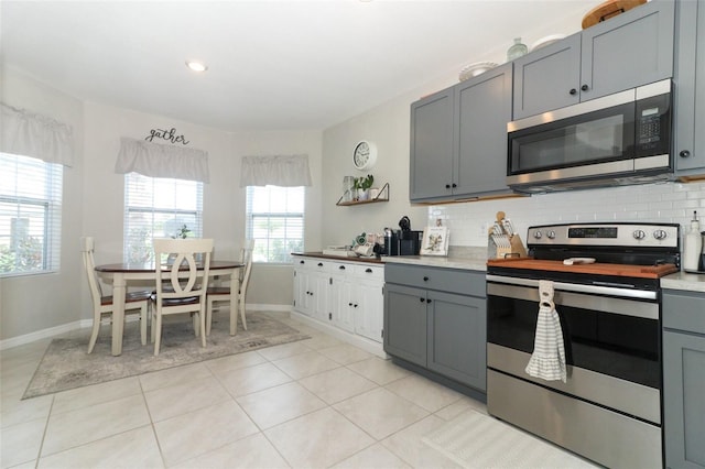 kitchen featuring backsplash, gray cabinetry, light tile patterned floors, and appliances with stainless steel finishes