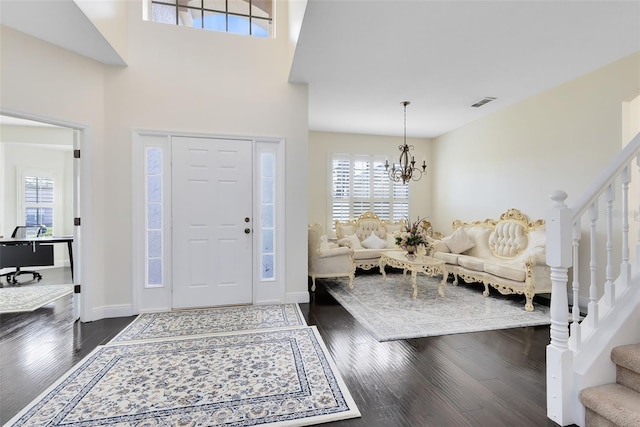 entryway with a towering ceiling, dark hardwood / wood-style floors, and an inviting chandelier