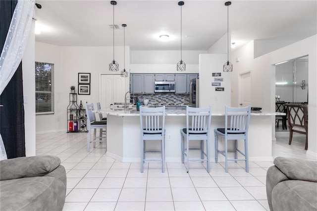 kitchen featuring pendant lighting, gray cabinetry, appliances with stainless steel finishes, tasteful backsplash, and a kitchen bar