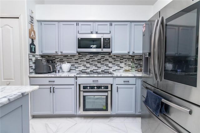 kitchen featuring decorative backsplash, light stone counters, gray cabinetry, and appliances with stainless steel finishes