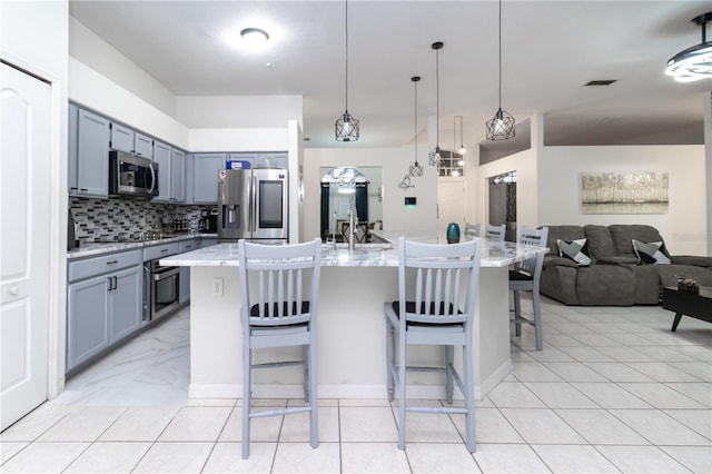 kitchen featuring stainless steel appliances, tasteful backsplash, an island with sink, pendant lighting, and a breakfast bar