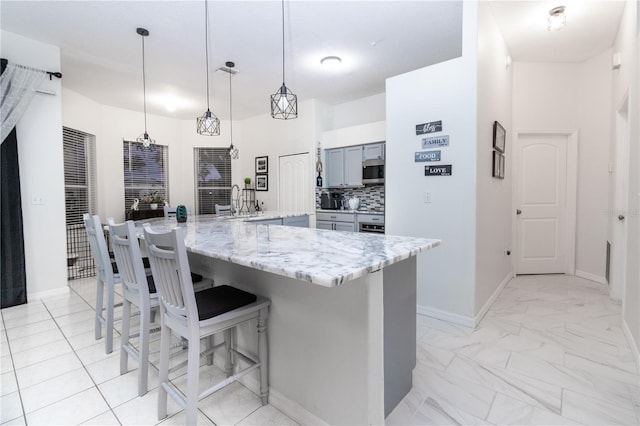 kitchen with light stone countertops, backsplash, a center island, hanging light fixtures, and a breakfast bar area