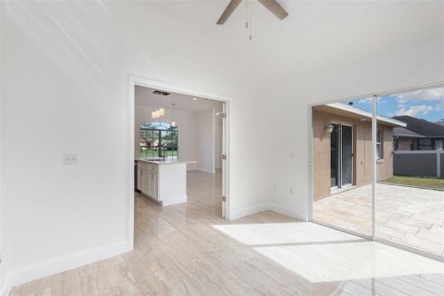 unfurnished room featuring ceiling fan with notable chandelier, sink, high vaulted ceiling, and light hardwood / wood-style flooring