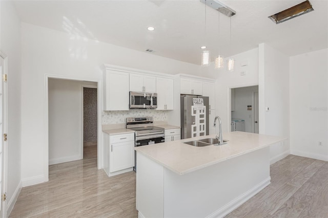 kitchen featuring washing machine and dryer, white cabinetry, an island with sink, and appliances with stainless steel finishes