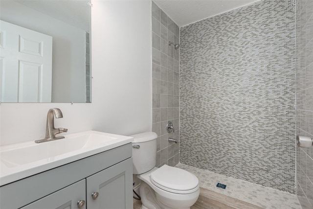 bathroom featuring a tile shower, vanity, hardwood / wood-style flooring, and toilet