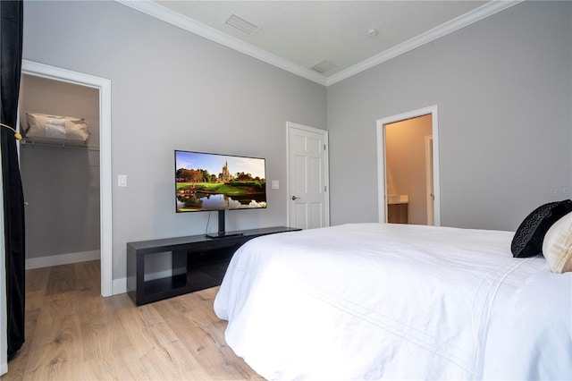 bedroom featuring light wood-type flooring, ensuite bath, ornamental molding, a spacious closet, and a closet