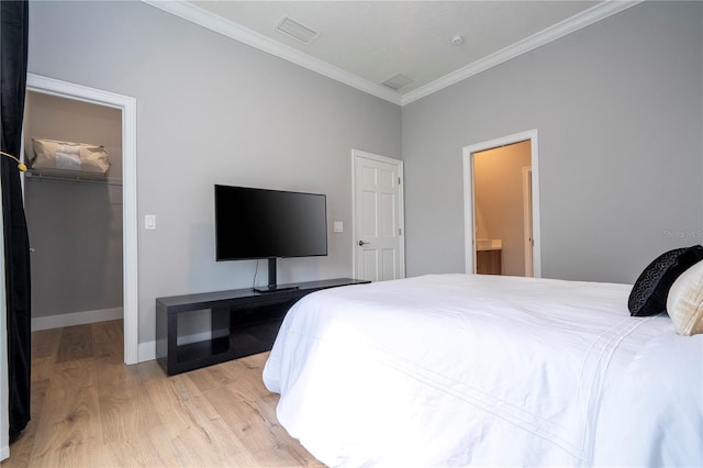 bedroom featuring light wood-type flooring, a walk in closet, ornamental molding, connected bathroom, and a closet