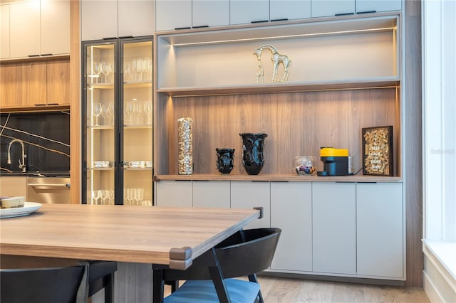 kitchen with a breakfast bar area, sink, white cabinets, and light wood-type flooring