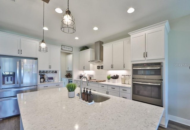 kitchen with stainless steel appliances, pendant lighting, wall chimney exhaust hood, light stone countertops, and white cabinetry