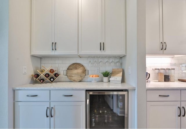 bar featuring wine cooler, tasteful backsplash, light stone counters, and white cabinets