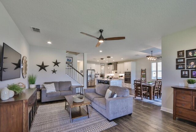 living room with dark hardwood / wood-style flooring, a textured ceiling, and ceiling fan with notable chandelier