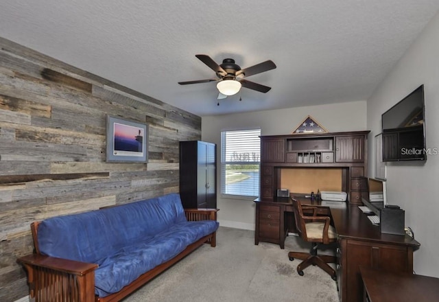 office area featuring a textured ceiling, light colored carpet, wooden walls, and ceiling fan