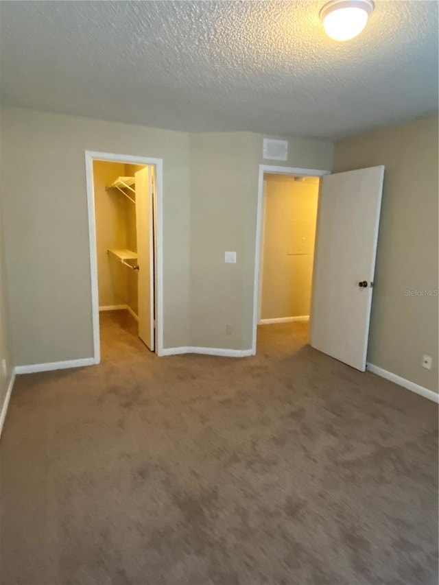 unfurnished bedroom with a closet, a walk in closet, a textured ceiling, and carpet