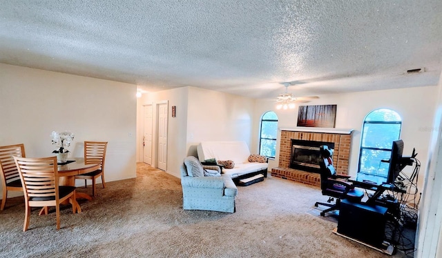 living room with ceiling fan, a fireplace, a textured ceiling, and carpet flooring