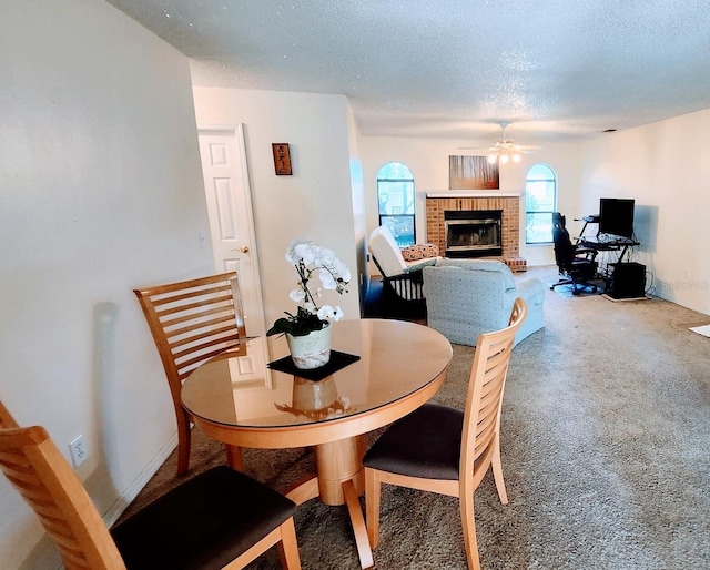 dining space featuring a brick fireplace, carpet floors, a textured ceiling, and ceiling fan