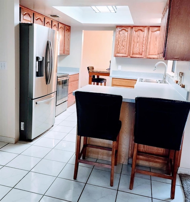 kitchen with light tile patterned flooring, appliances with stainless steel finishes, a breakfast bar, sink, and kitchen peninsula