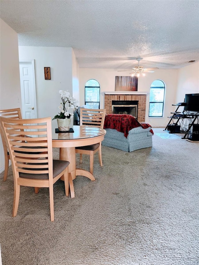 carpeted dining room featuring ceiling fan, a brick fireplace, and a textured ceiling