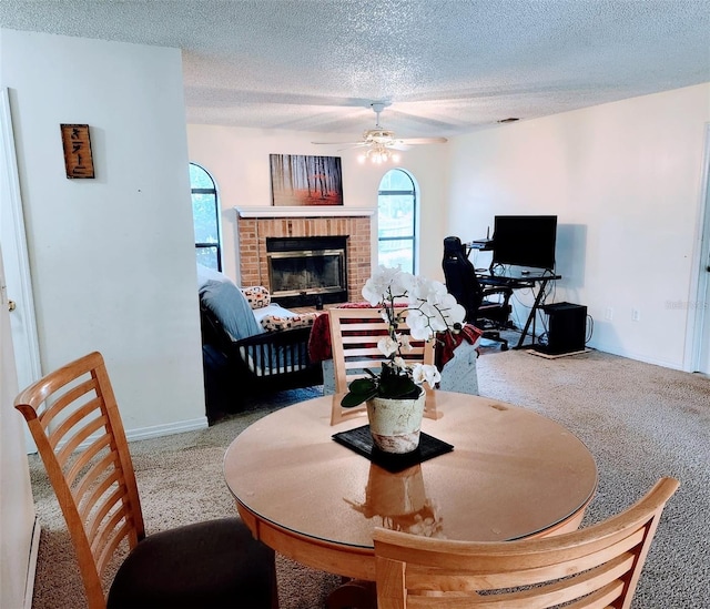 carpeted dining room with a brick fireplace, a textured ceiling, and ceiling fan