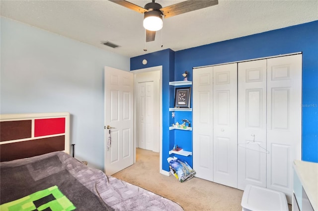 bedroom featuring a textured ceiling, light colored carpet, a closet, and ceiling fan