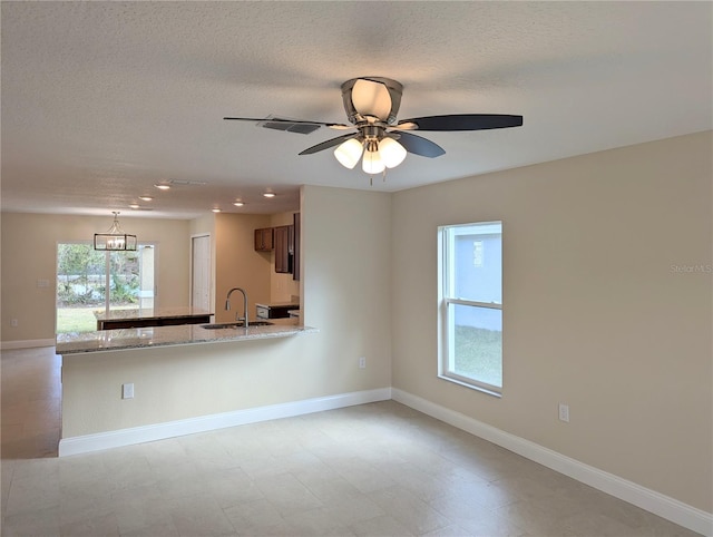 interior space featuring kitchen peninsula, light stone counters, ceiling fan, and sink