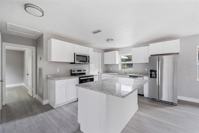 kitchen featuring light stone counters, a center island, white cabinetry, appliances with stainless steel finishes, and light hardwood / wood-style flooring