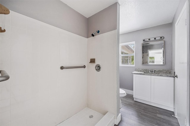 bathroom featuring wood-type flooring, vanity, toilet, and tiled shower