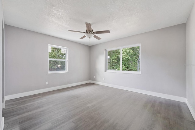 empty room with ceiling fan, a wealth of natural light, dark hardwood / wood-style floors, and a textured ceiling