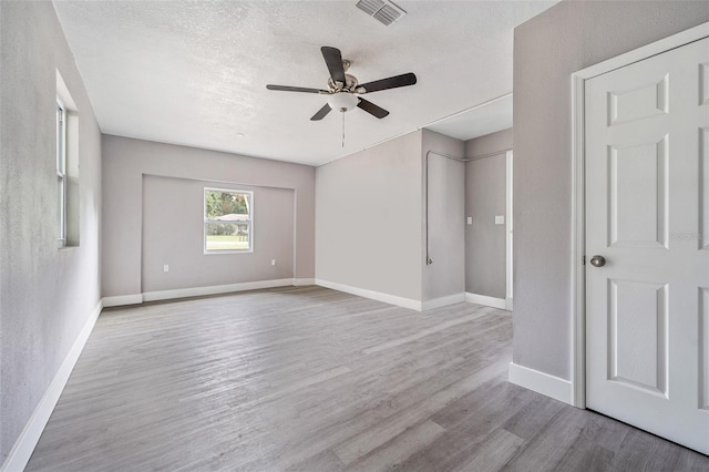 unfurnished room with a textured ceiling, light wood-type flooring, and ceiling fan